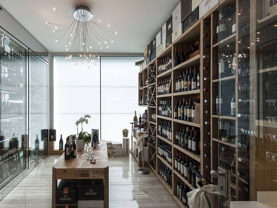 A wine cellar with shelves of wine bottles, a central display table with wine glasses, and a modern chandelier.