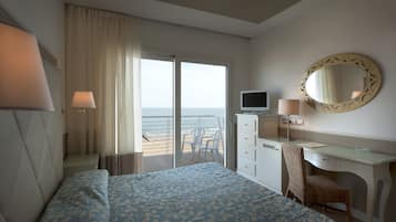 A hotel room with a bed, a desk, a chair, a television, and a large window with a view of the sea.