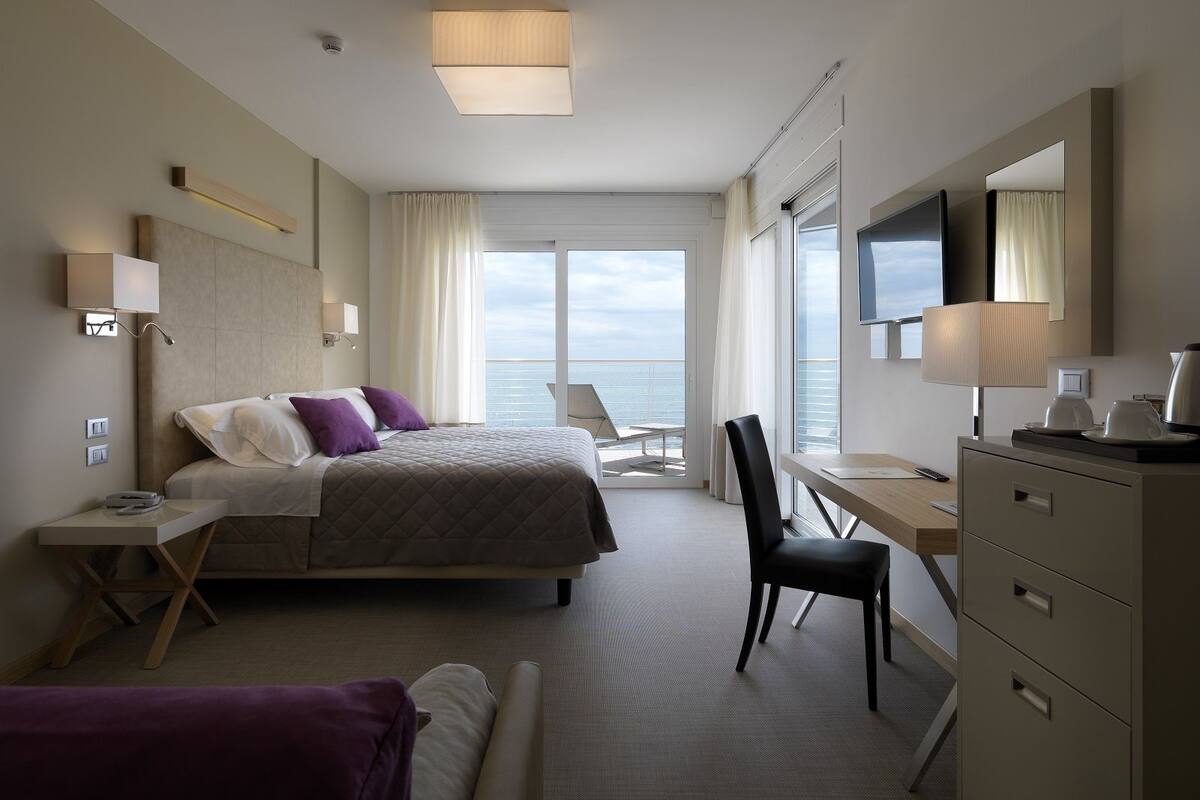 Ett modernt hotellrum med en säng, ett skrivbord, en stol och utsikt över havet.