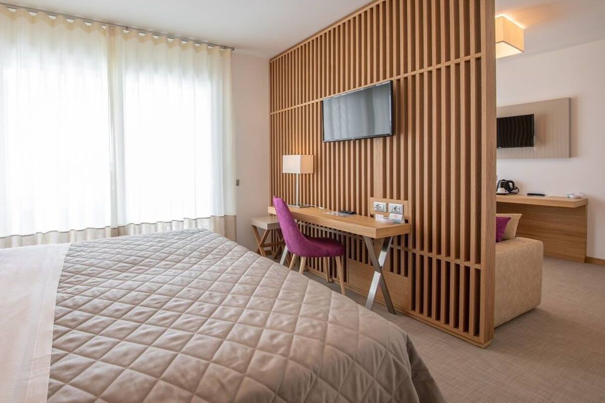 Ett hotellrum med en stor säng, ett skrivbord, en stol, en tv och ett fönster med gardiner.
