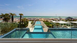 A pool area with clear blue water, a beach with umbrellas and lounge chairs, and a view of the ocean. - Hotel Le Soleil (Jesolo)