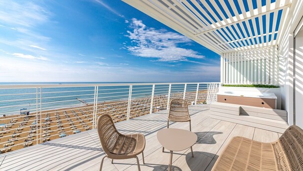 A balcony with wicker furniture, a view of the beach, and a white pergola. - Hotel Le Soleil (Jesolo)