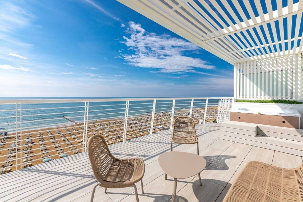 En balkong med möbler i rotting, utsikt över stranden och en vit pergola.