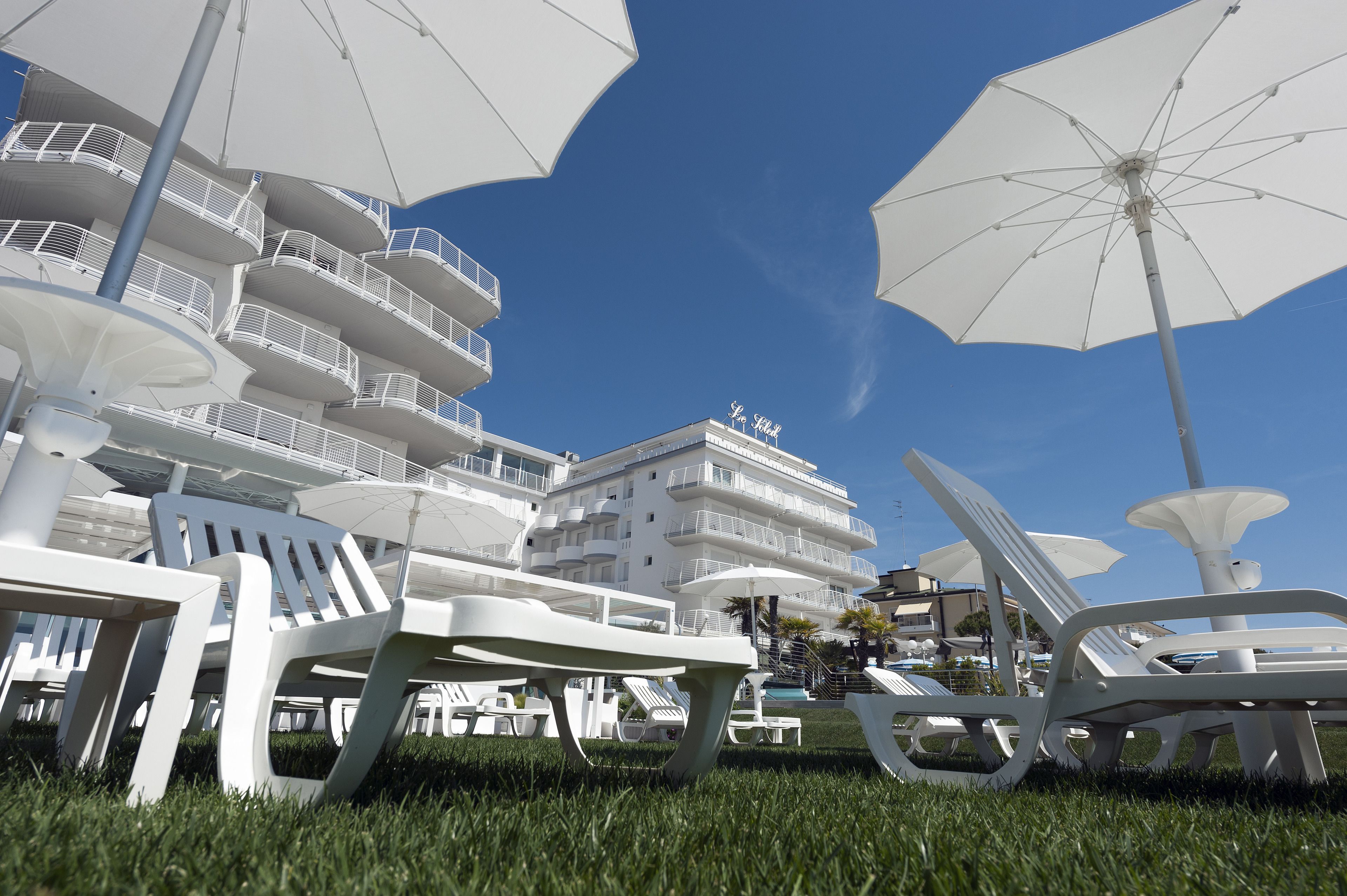 Un hôtel doté de nombreux balcons, d’un espace extérieur aménagé avec des sièges et de parasols.