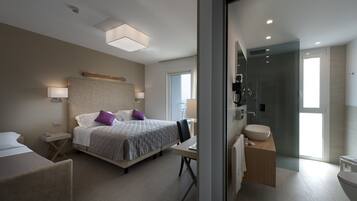 Una moderna camera d'albergo con un letto grande, una scrivania e un bagno con doccia in vetro.