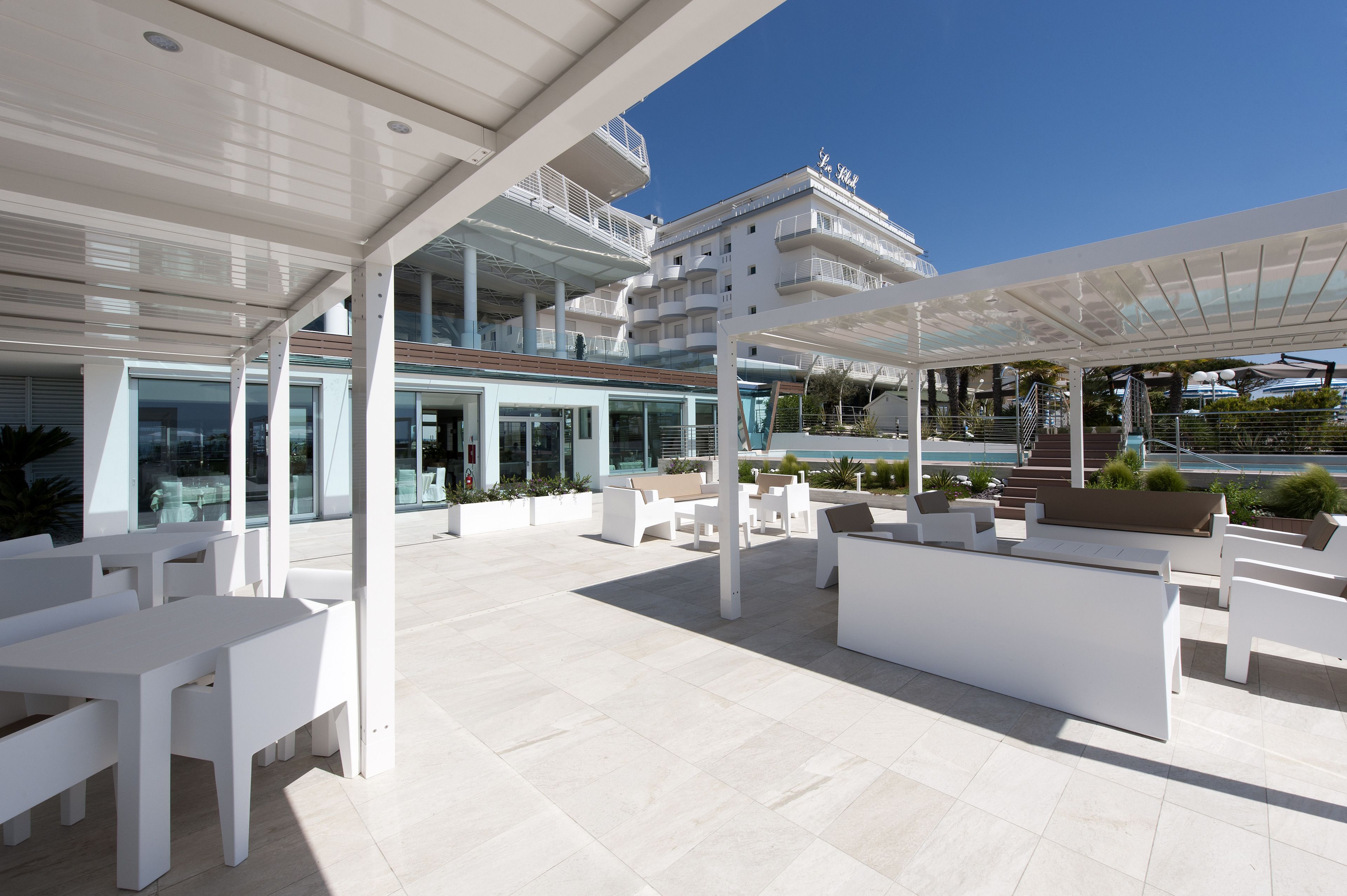A modern outdoor lounge area with white furniture and a glass balustrade overlooking a pool.