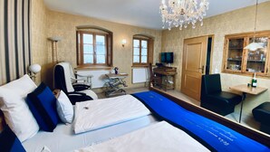 A hotel room with a bed, a desk, a chair, a television, and a chandelier. - Haus am Markt (Königstein)