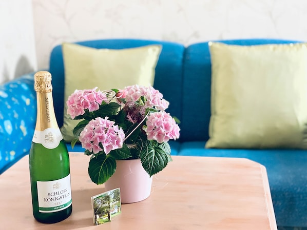 A bottle of SCHLOSS KÖNIGSTEIN Sekt, a pink hydrangea plant, and a small photograph on a wooden table.