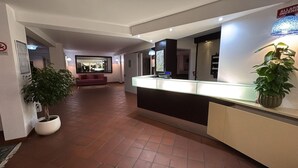 A reception area with a counter, potted plants, a mirror, and a sign indicating an all-alarms system.