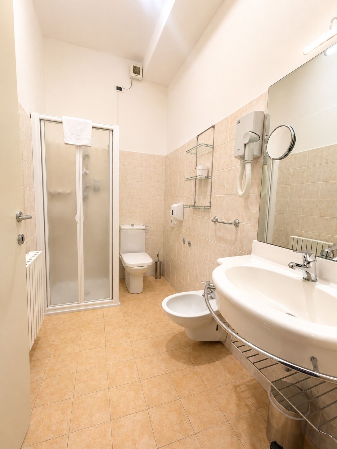 Un baño con cabina de ducha de vidrio, inodoro, bidé, lavamanos con espejo y toallero.