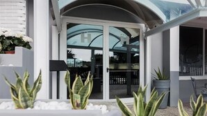 A modern building with a glass entrance, potted plants, and a metal railing.