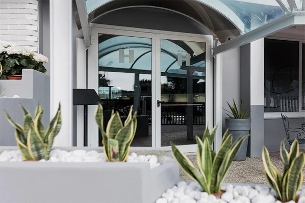 A modern building with a glass entrance, potted plants, and a metal railing. - Hotel Eurovil Panoramic View (Predore)