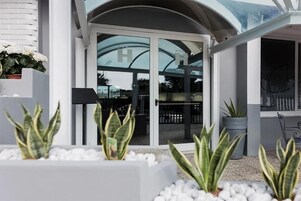 Un edificio moderno con entrada de vidrio, plantas en macetas y barandilla de metal.