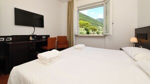 A hotel room with a bed, a desk with a flat-screen TV, a chair, and a window with a mountain view.