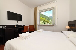 Habitación de hotel con cama, escritorio con televisor de pantalla plana, silla y ventana con vista a la montaña.