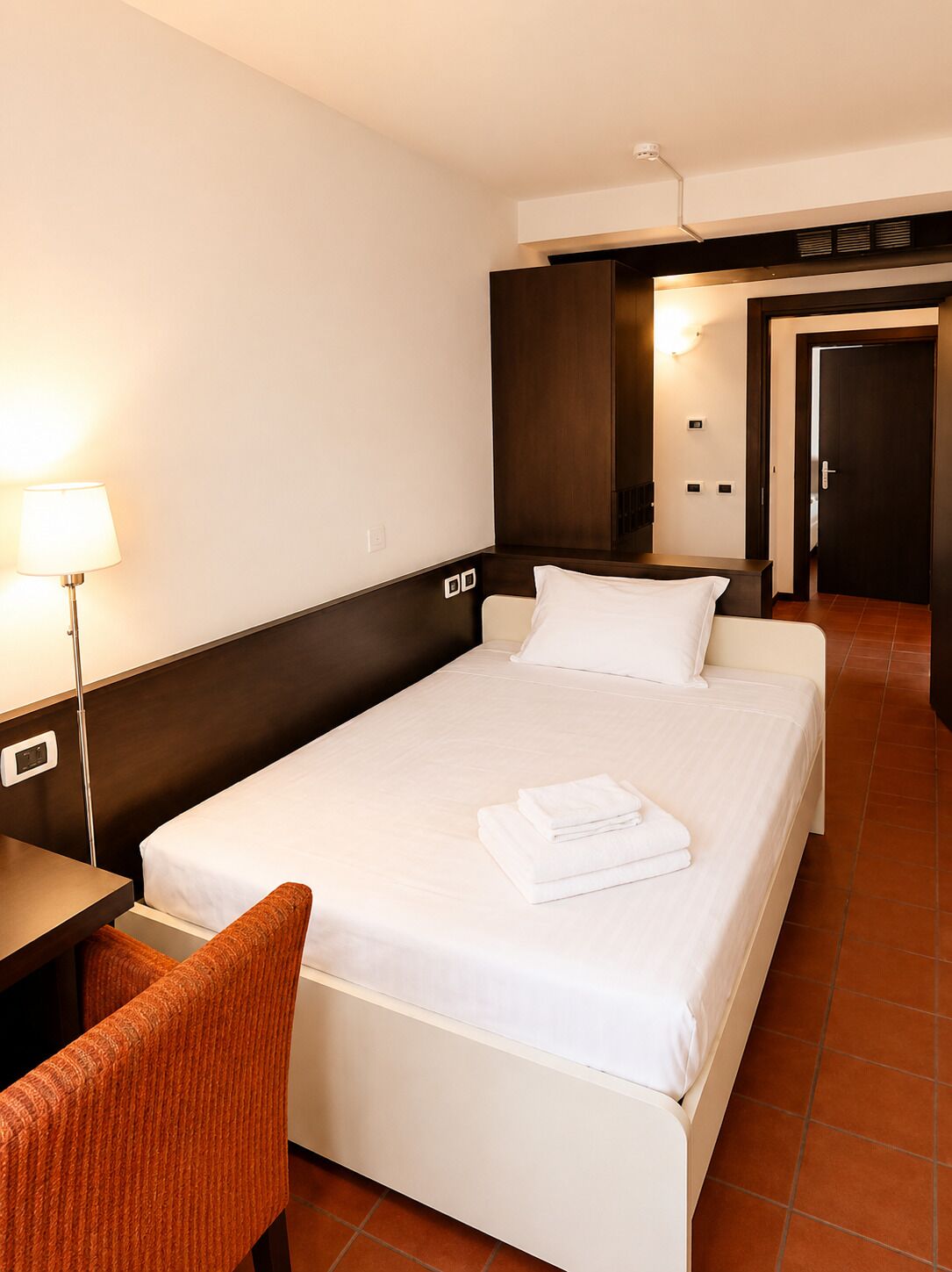 Ein Hotelzimmer mit Bett, Schreibtisch, Stuhl, Lampe und einer Tür.