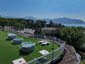 A rooftop terrace with multiple hot tubs, outdoor seating, and a view of the sea and mountains.