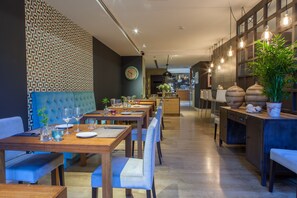 Un restaurante con mesas y sillas de madera, un muro con diseño y luces colgantes.