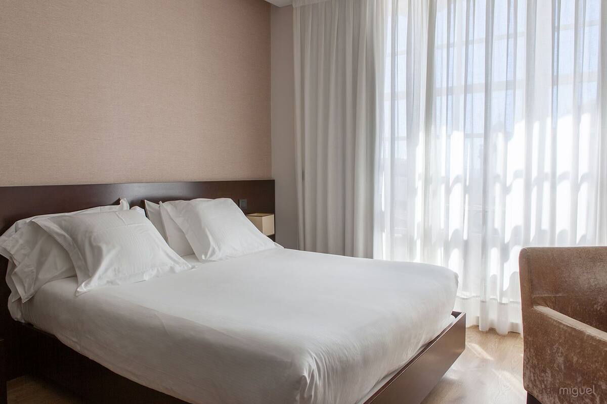 A hotel room with a large bed, a wooden headboard, a nightstand, and a chair.