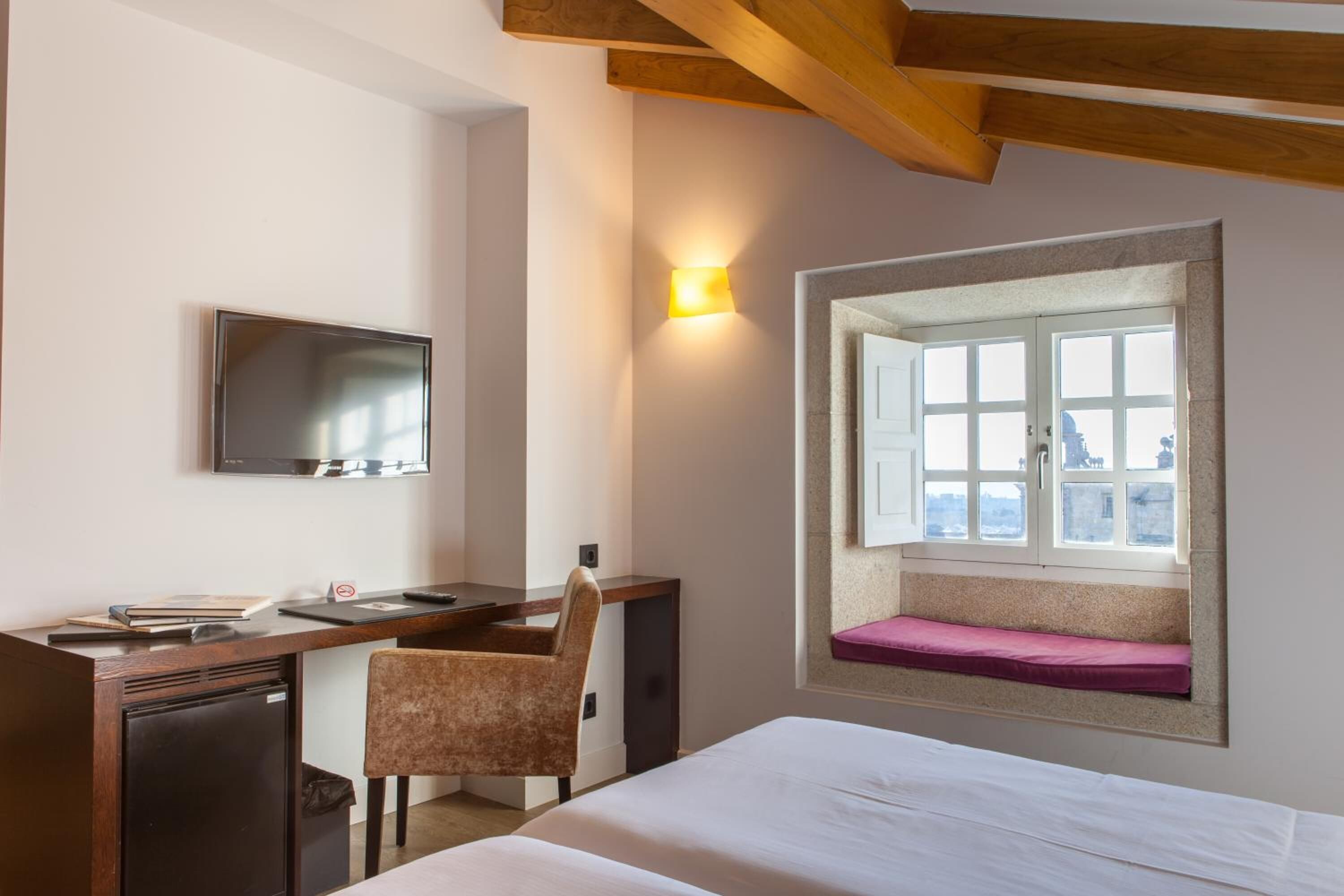 Una habitación de hotel con una cama, un escritorio, una silla, un televisor y una ventana con vistas.