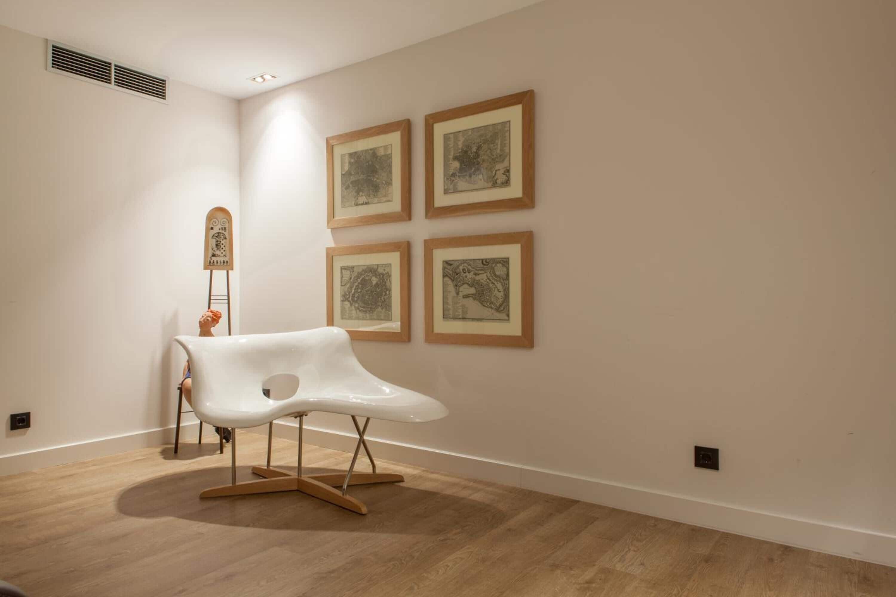 A modern art gallery with a white chair, four framed artworks on the wall, and a wooden sculpture.