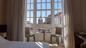 Habitación de hotel con una ventana grande, dos sillones, una mesita y una cama.