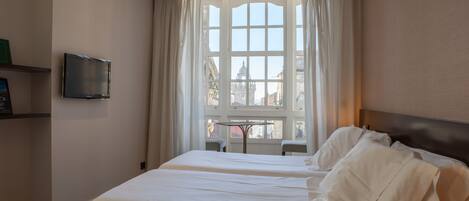 Una habitación de hotel con una cama grande, un televisor en la pared y una ventana con cortinas.