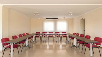 Un salón de conferencias con una larga mesa y sillas rojas, ventanas amplias con persianas y un equipo de aire acondicionado instalado en el techo.