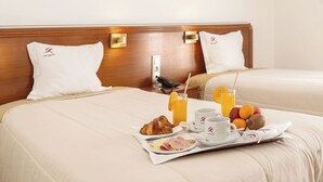 A hotel room with a neatly made bed, a tray with breakfast including croissant, fruits, juice, and coffee cups. - Hotel Comendador (Bombarral)