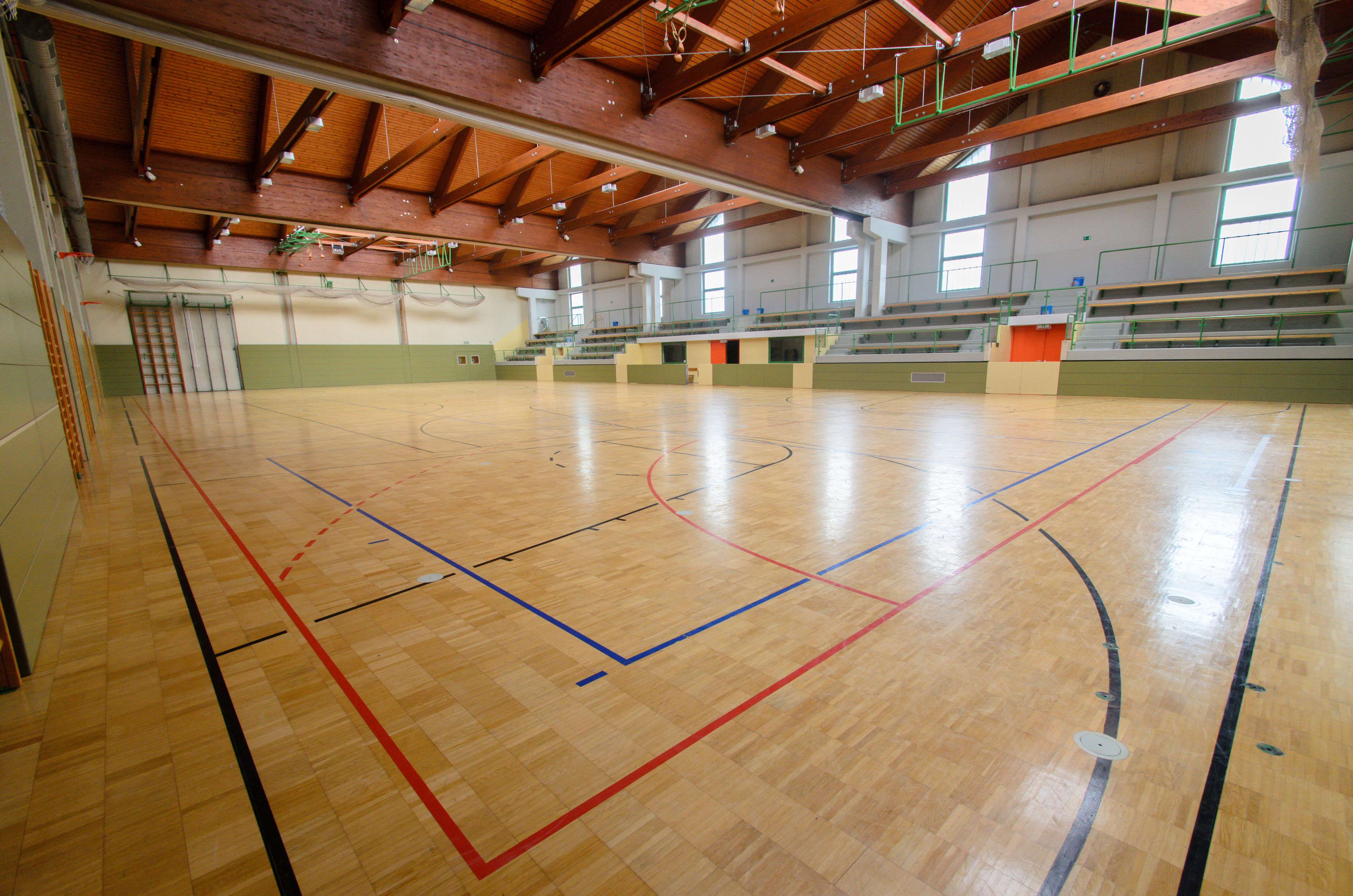 En indendørs sportshal med trægulv, basketballbanemarkeringer og tilskuerpladser.