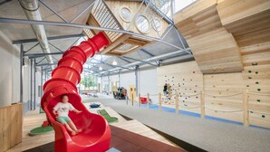 Uma área de recreação infantil com um escorrega vermelho, paredes de escalada e um parquinho.
