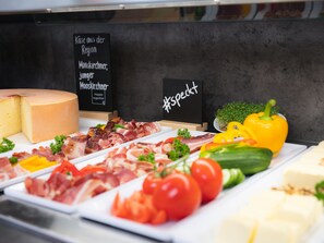Um queijo inteiro, diversos tipos de carne e legumes expostos.