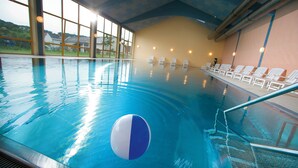 Uma piscina interior com água cristalina, uma bola flutuando e espreguiçadeiras à beira da piscina.