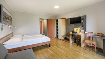 Quarto de hotel com cama, escrivaninha, cadeira, televisão e guarda-roupa.