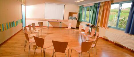 A conference room with a round table, chairs, a projector screen, and windows with curtains.