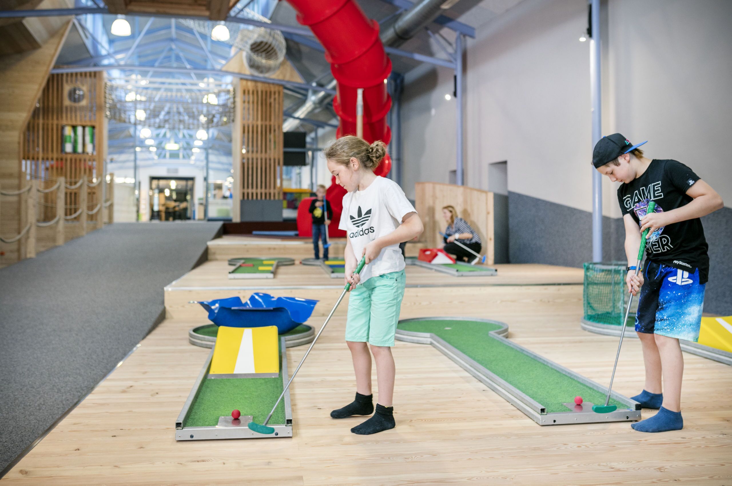 An indoor mini-golf course with wooden flooring and artificial turf.