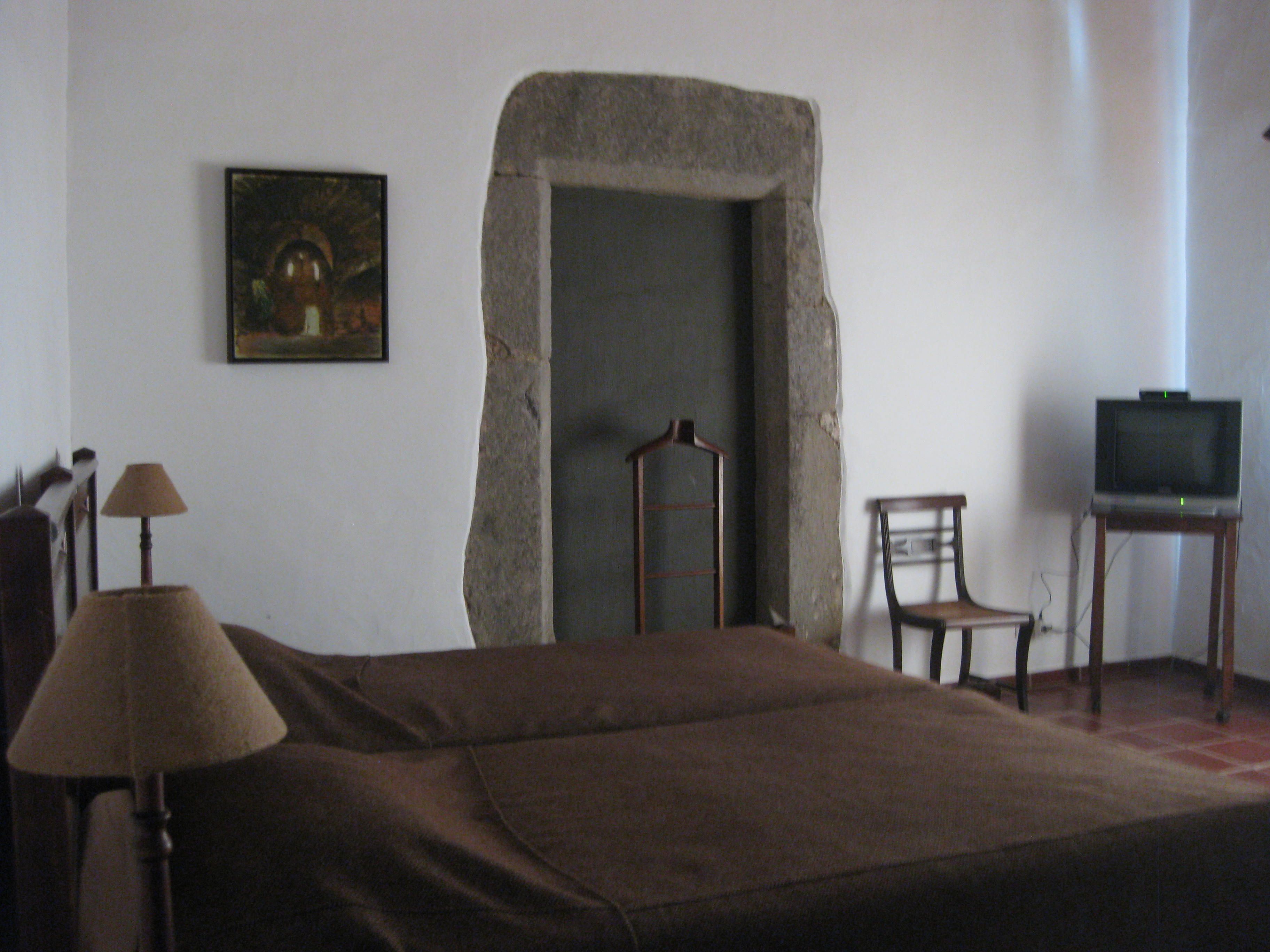 A room with a bed, a chair, a television, a lamp, and a painting on the wall.