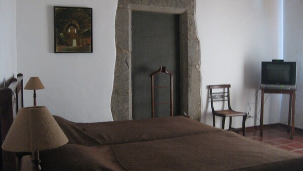 A room with a bed, a chair, a television, a lamp, and a painting on the wall.