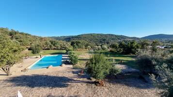 Zona de piscina con un patio de piedra, rodeada de árboles y colinas al fondo.