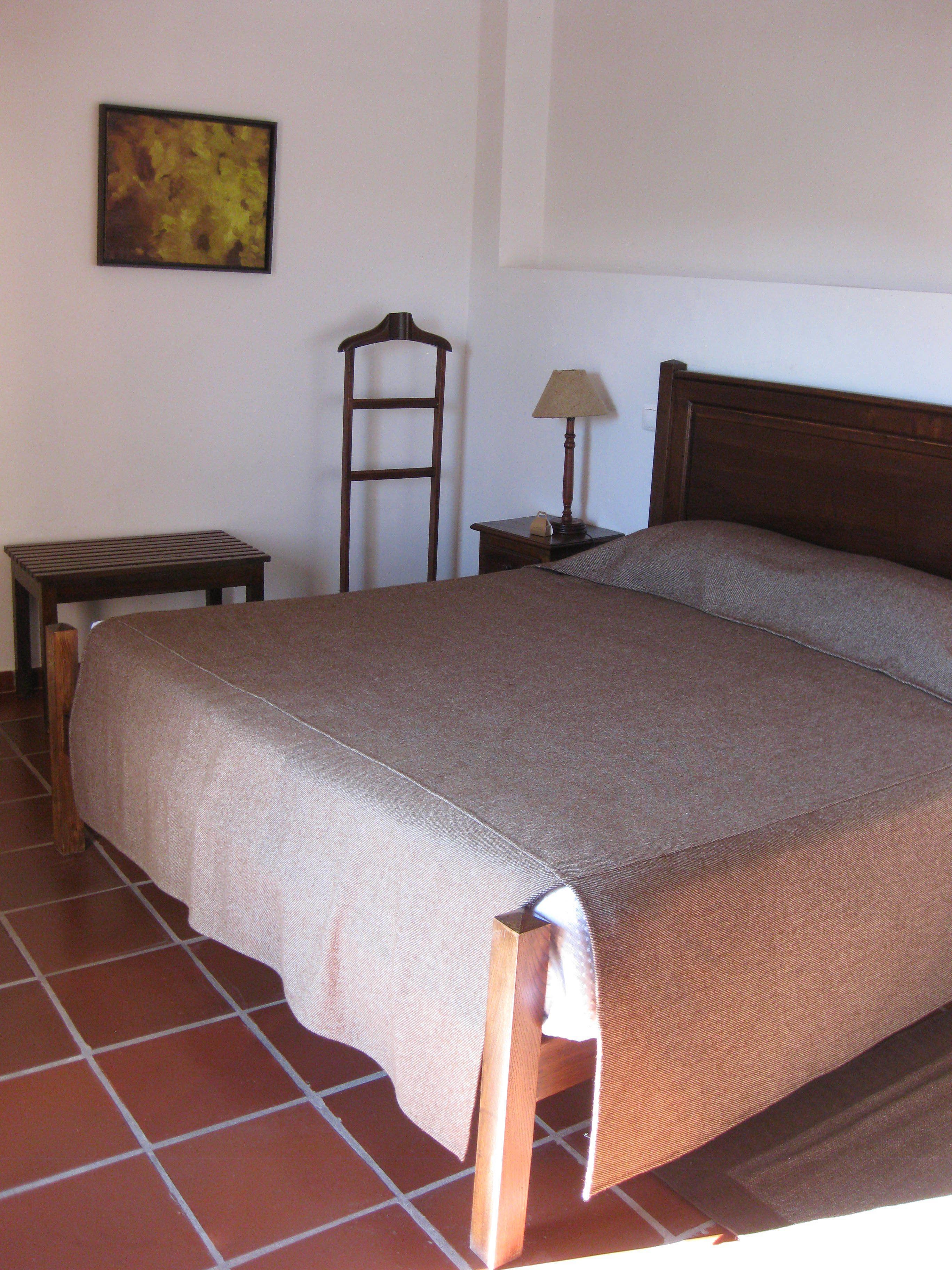 A bedroom with a bed, a nightstand, a lamp, a chair, and a painting on the wall.