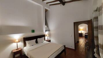A bedroom with a large bed, wooden beams on the ceiling, and a small table with a lamp.