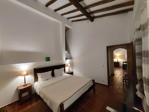 A bedroom with a large bed, wooden beams on the ceiling, and a small table with a lamp.