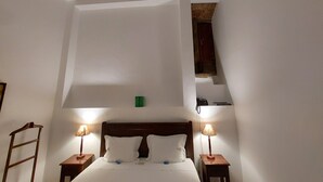 Une chambre à coucher comprenant un lit, deux tables de chevet avec des lampes, une tête de lit en bois et un plafond en pente avec des poutres en bois.