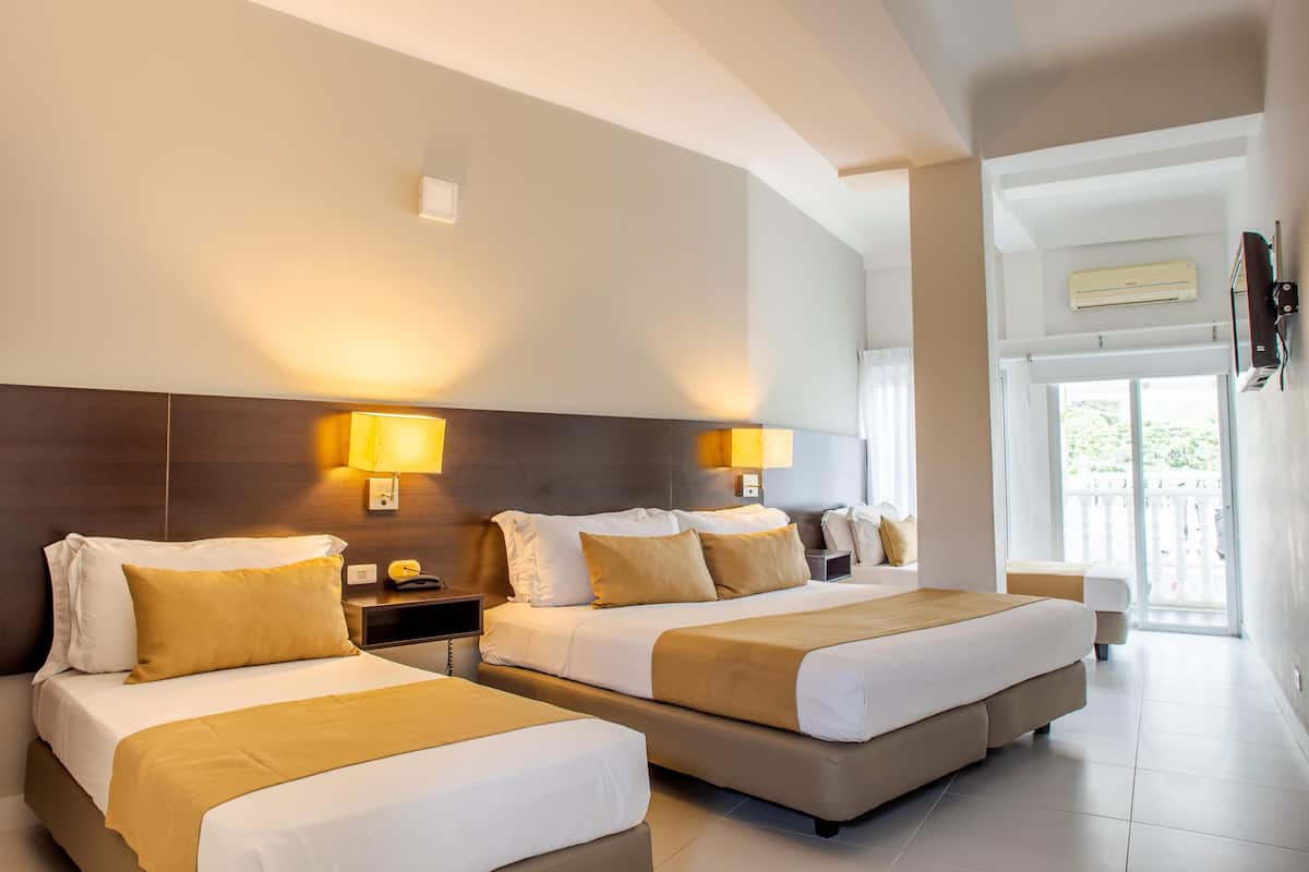 A hotel room with two beds, a nightstand, a lamp, and a view of the outdoors.