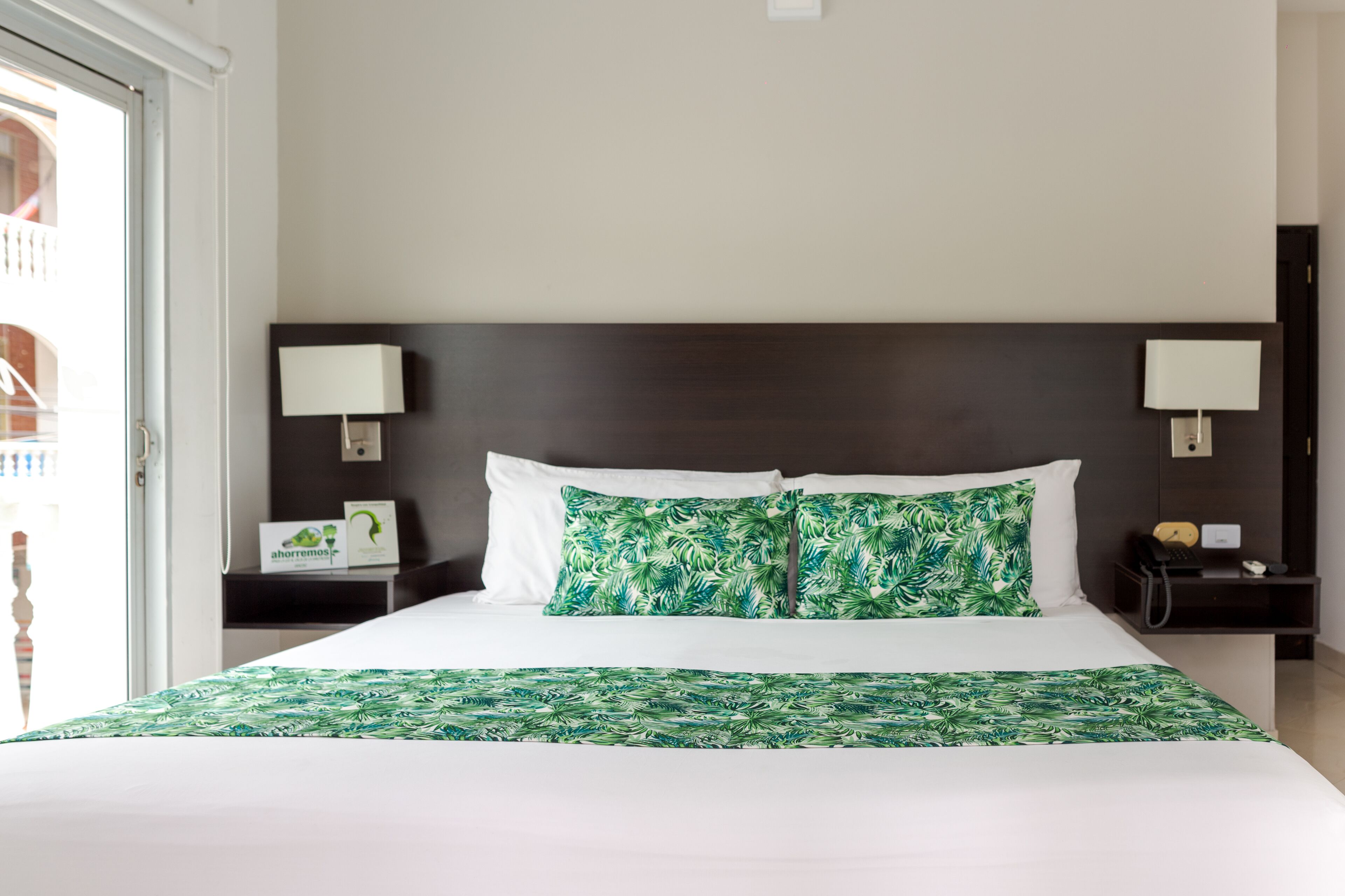 A hotel room with a large bed, two bedside tables, a nightstand, and a view of the outside balcony.