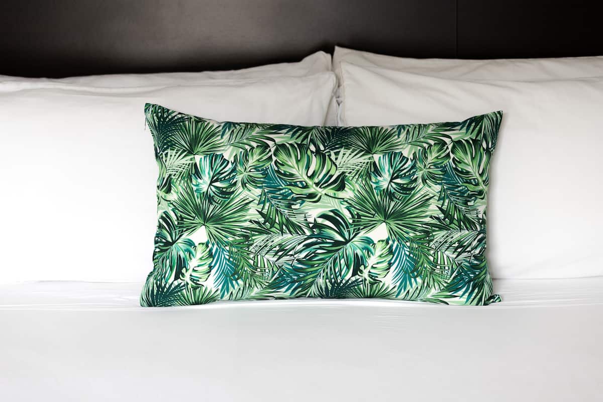 A bed with white linens and a single green leaf-patterned pillow.