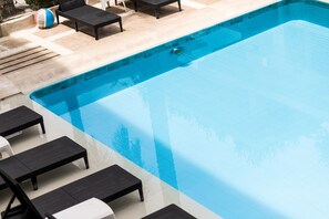 Una piscina con sillas reclinables negras y un deck de baldosas.
