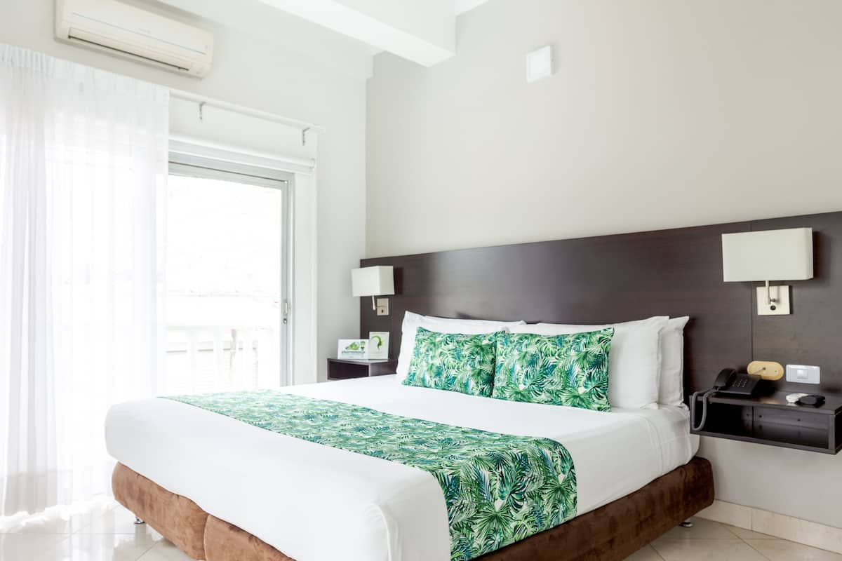 A hotel room with a large bed, a bedside table with a lamp, a phone, and a small shelf.