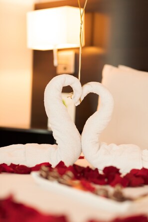 Una cama con toallas dispuestas en forma de corazón y pétalos de rosa.