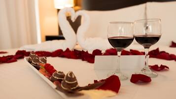 A bed with rose petals, two wine glasses, and a chocolate dessert tray.